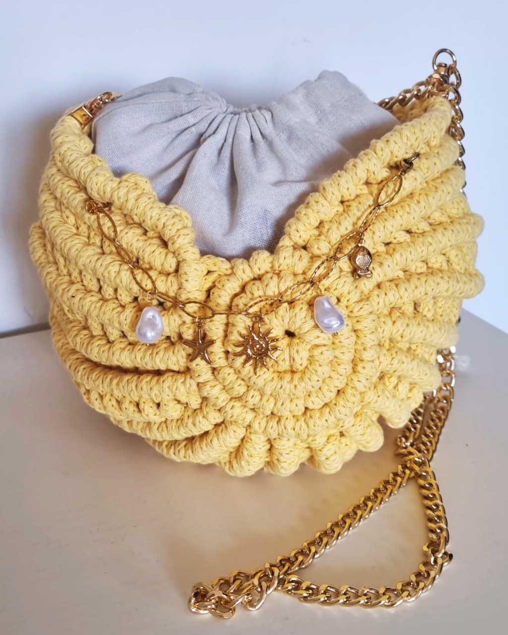 Bolsa Búzio Amarelo Manteiga - detalhe dos charms: estrela do mar e sol dourado com pérolas barrocas