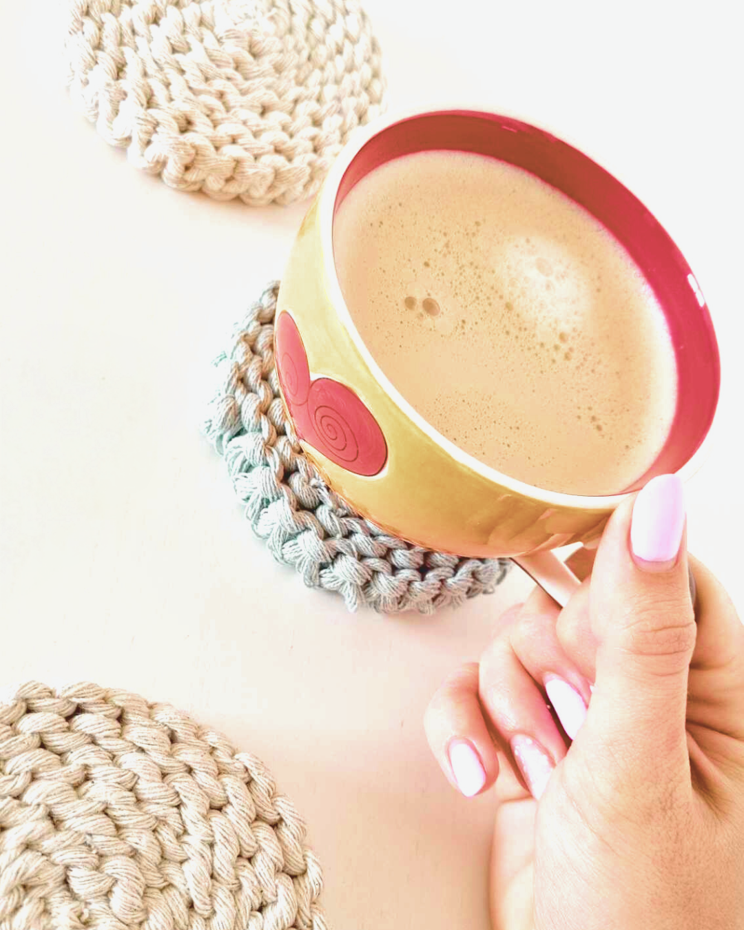 Mão a segurar chávena de café sobre base circular em macramé colorido — peça artesanal do curso Mãos em Terapia | Jungle Macramé
